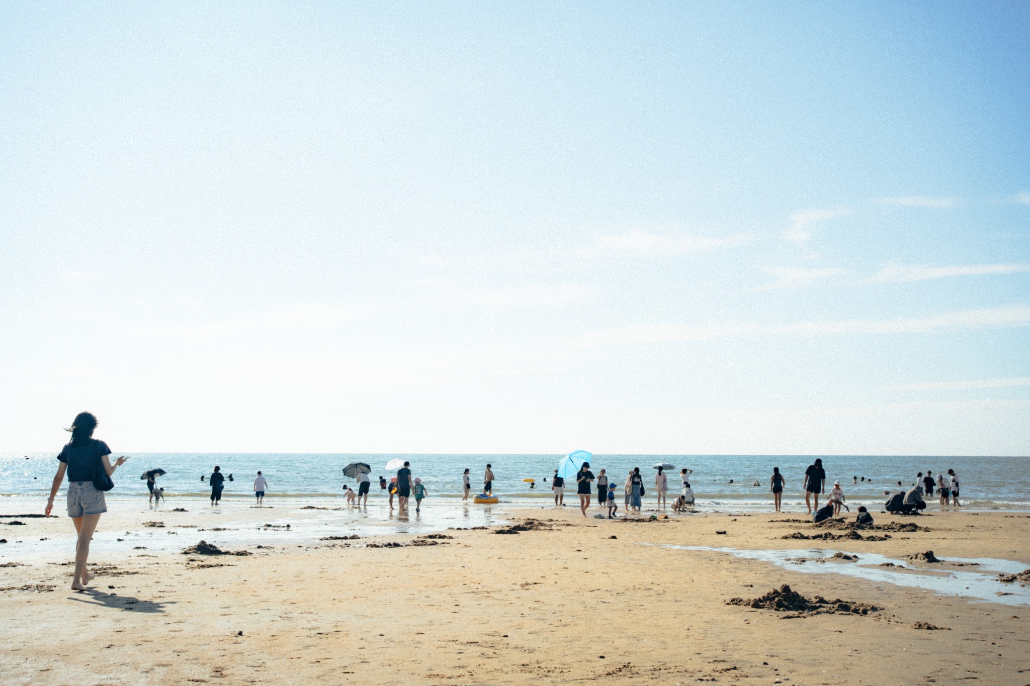 People wading along a sunlit sandy beach