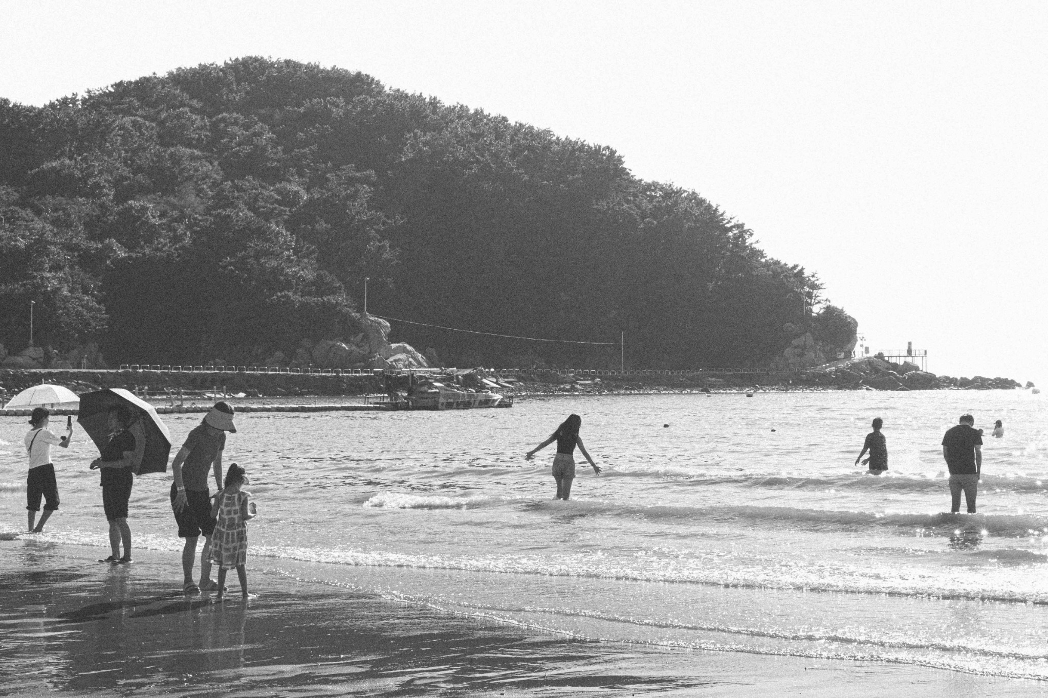 Beachgoers walking through shallow water in black and white